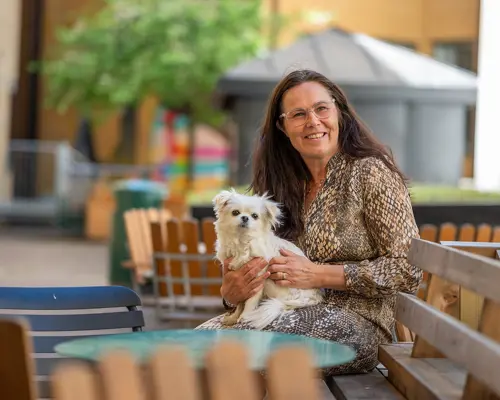 Kvinna med en vit hund i famnen på en innegård